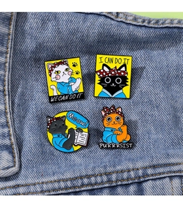 Detailed view of four cat enamel pins with motivational quotes on blue denim jacket