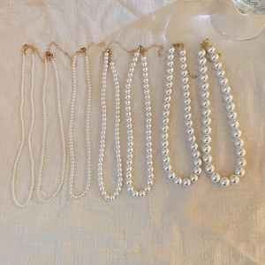 Detail view of multi-size white pearl necklaces with adjustable gold-tone metal clasps