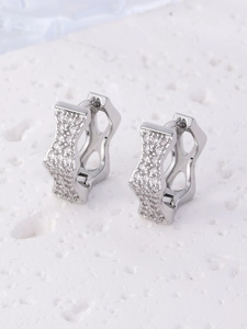 Macro shot of silver pavé crystal hoop earrings with geometric cutouts on stone background