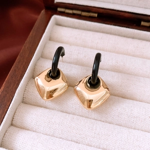 Macro view of geometric gold square pendants on black hooks in a velvet gift box