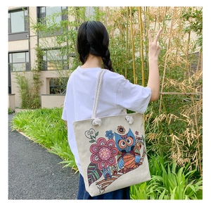 Detailed back view of a beige canvas tote bag with owl embroidery in a bamboo garden