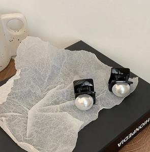 Detailed view of two minimalist black hair clips with white pearls on artistic paper