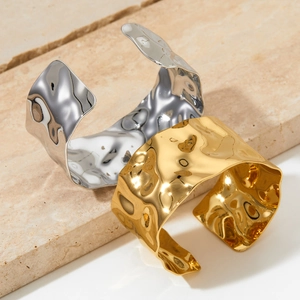 Minimalist wide hammered stainless steel bangles in gold and silver on a stone surface