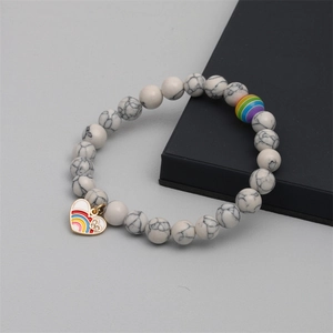 Close-up of white howlite beaded bracelet with a gold heart-shaped rainbow charm