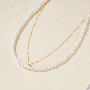 Detail of double-layer necklace featuring white pearls, gold chain, and solitaire pendant
