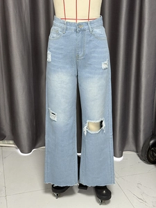 Detail of high waisted wide leg light blue denim jeans with distressed knee rips and raw hem