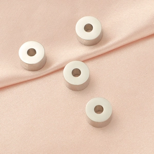 Detailed view of silver cylindrical beads for DIY jewelry on pink silk fabric