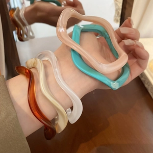 Detail of wavy resin bracelets in amber and assorted colors worn on wrist in a warm setting