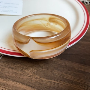 Detail of amber acrylic bangle showing brown marble texture on white porcelain plate
