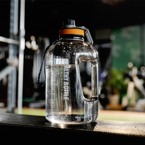 Detail of a large gradient sports bottle with orange lid and handle in a gym setting