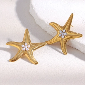 Textured 18K gold plated starfish earrings with white pearls on a sand background