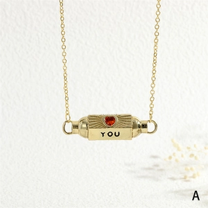 Close-up of golden necklace with a red heart gemstone and engraved YOU inscription