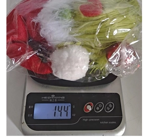 Detail view of a Grinch-style gnome plush on a digital scale showing 144g weight