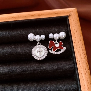 Detail of asymmetric pearl earrings featuring red rocking horse and cross pendant charms