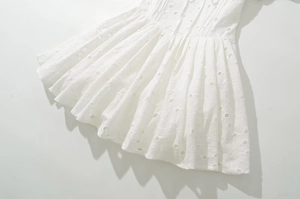 Détail d'une robe en coton blanc avec broderie ajourée délicate et texture plissée élégante