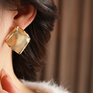 Gros plan de grandes boucles d'oreilles carrées dorées avec texture de grille fine