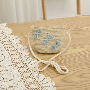 Detail of hand-woven straw crossbody bag featuring light blue lace bows and a cotton rope strap