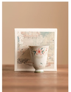 Macro shot of hand-painted peach blossom ceramic teacup with elegant calligraphy gift box