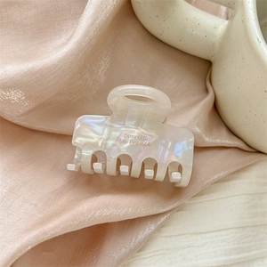 Close-up of pearl white iridescent acetate hair claw clip on pink silk background