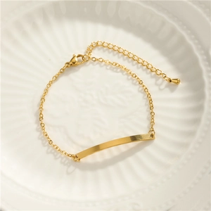 Close-up of golden curved bar bracelet with fine chain on a wavy white plate