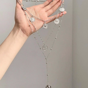 Detail of silver multilayered necklace with multiple embossed coin pendants in hand