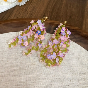 Colorful floral fringe earrings with sequins and beads on a rustic wooden tray