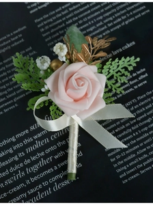 Detail of pink foam rose boutonniere with gold leaves and ivory ribbon for weddings