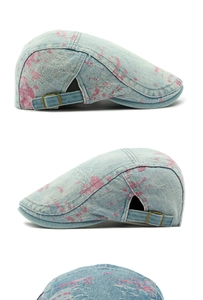 Detailed view of washed denim flat cap with pink splatter paint and bronze metal buckle