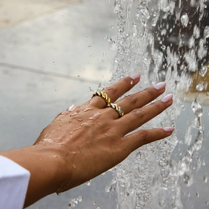 Twisted two-tone and gold stainless steel rings worn by model under splashing water