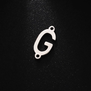 Macro view of a polished stainless steel letter G pendant with top and bottom loops