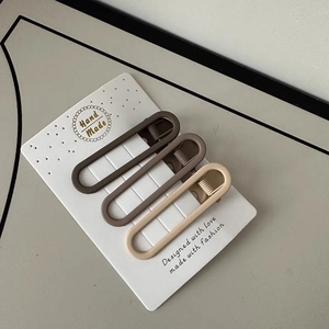 Close-up of three matte minimalist duckbill hair clips in brown and beige tones on a card