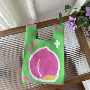 Detailed close-up of green knit tote bag with a pink peach pattern on a glass table