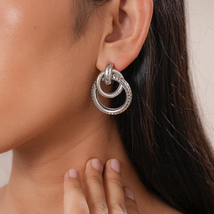 Macro view of interlocking silver geometric hoop earrings worn on a model ear