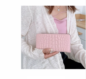 Lange rosa Damengeldbörse mit Kroko-Prägung, präsentiert von einem Model zu Hause