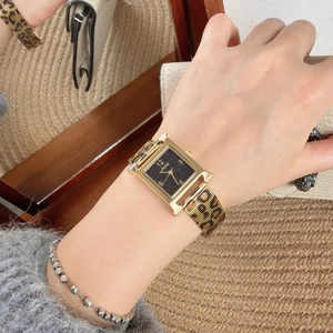 Detail of H-shaped gold watch with black starry dial and leopard print strap on wrist