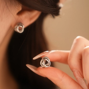Gros plan de boucles d'oreilles nœuds en métal argenté portées et tenues par un mannequin