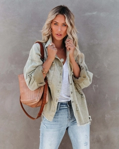 Close-up of distressed denim jacket featuring heavy frayed holes and metallic buttons