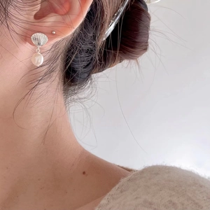 Close-up of elegant shell design silver earrings with white pearls worn by a model