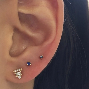Detailed close-up of blue gemstone studs and crystal butterfly earrings on cartilage
