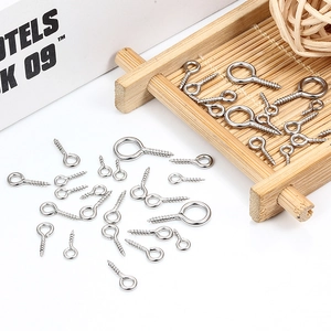 Polished stainless steel eye pin screws in various sizes on a wooden tray for DIY jewelry