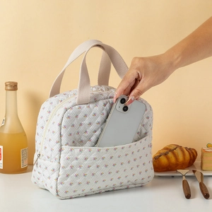 Detalle de bolsa térmica acolchada floral con un móvil en el bolsillo delantero.