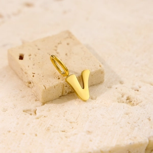 Detailed close-up of a golden V-shaped letter pendant on a natural stone surface