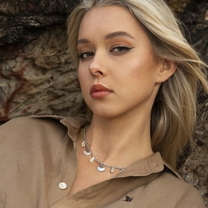 Model wearing a 18k gold ocean starfish necklace with shell charms against rock background