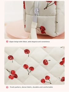 Macro detail of quilted white cosmetic bag with cherry patterns and ribbon zipper pull