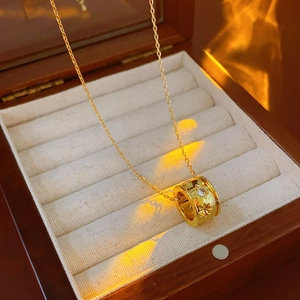 Dettaglio collana dorata con pendente a cilindro inciso a stelle e pietra di zircone