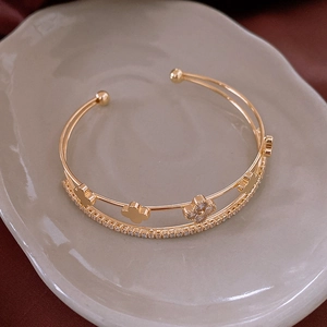 Detail of gold open bracelet with zircon four-leaf clover motifs and double-layered bands