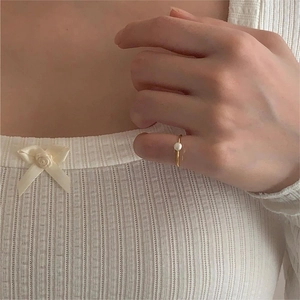 Close-up of a minimalist gold band ring with a single white pearl on a finger