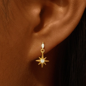 Macro shot of gold eight-point star drop earring with cubic zirconia on a model ear