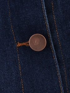 Gros plan sur un denim bleu foncé avec coutures orange et rivet métallique en bronze brossé