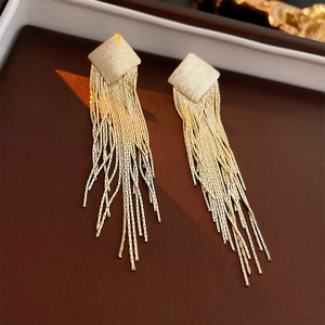 Macro view of gold rhombic fringe earrings featuring brushed metal square stud details